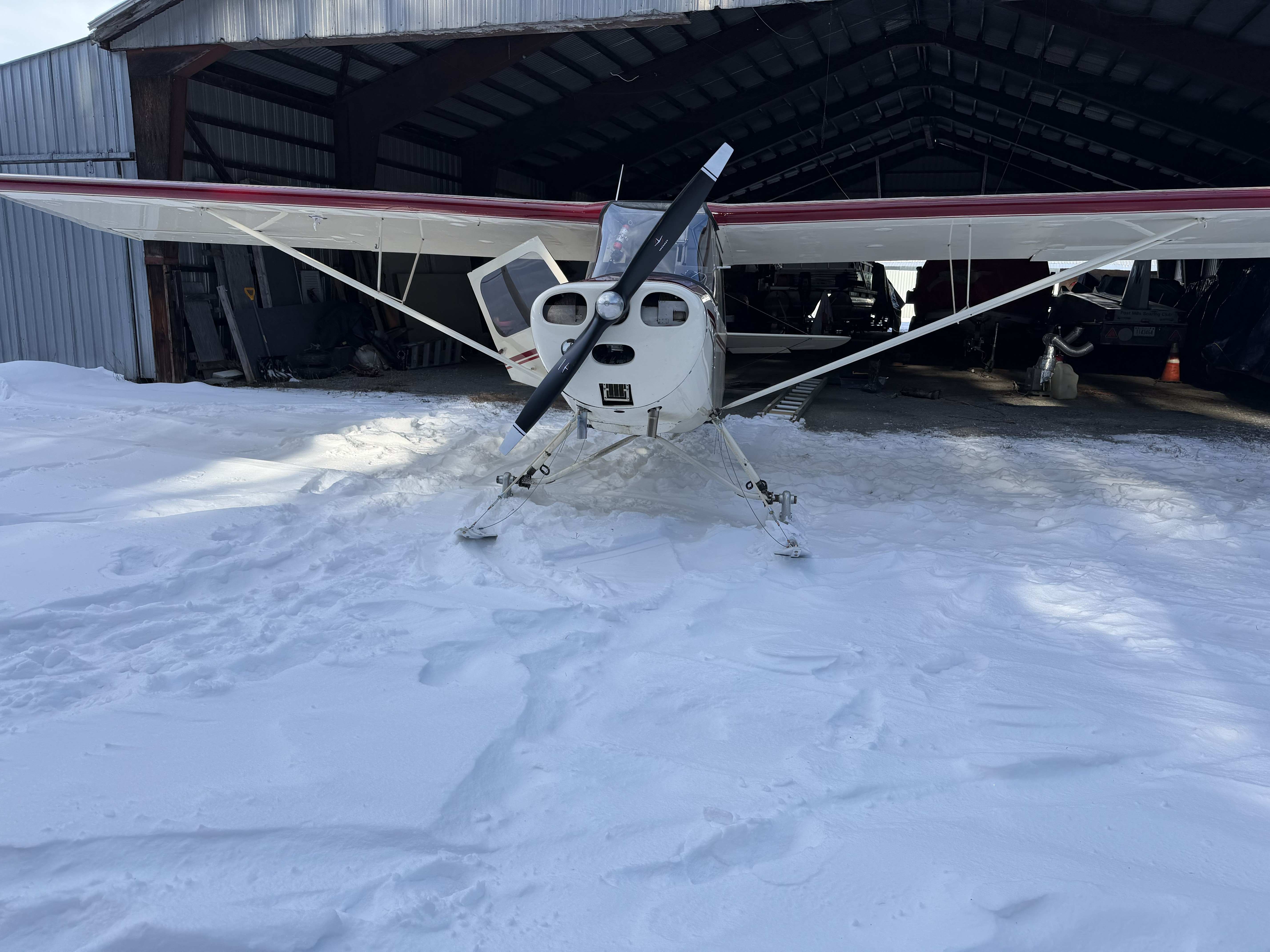 White ski plane parked in the snow in front of the Post Mills Airport hangar in winter