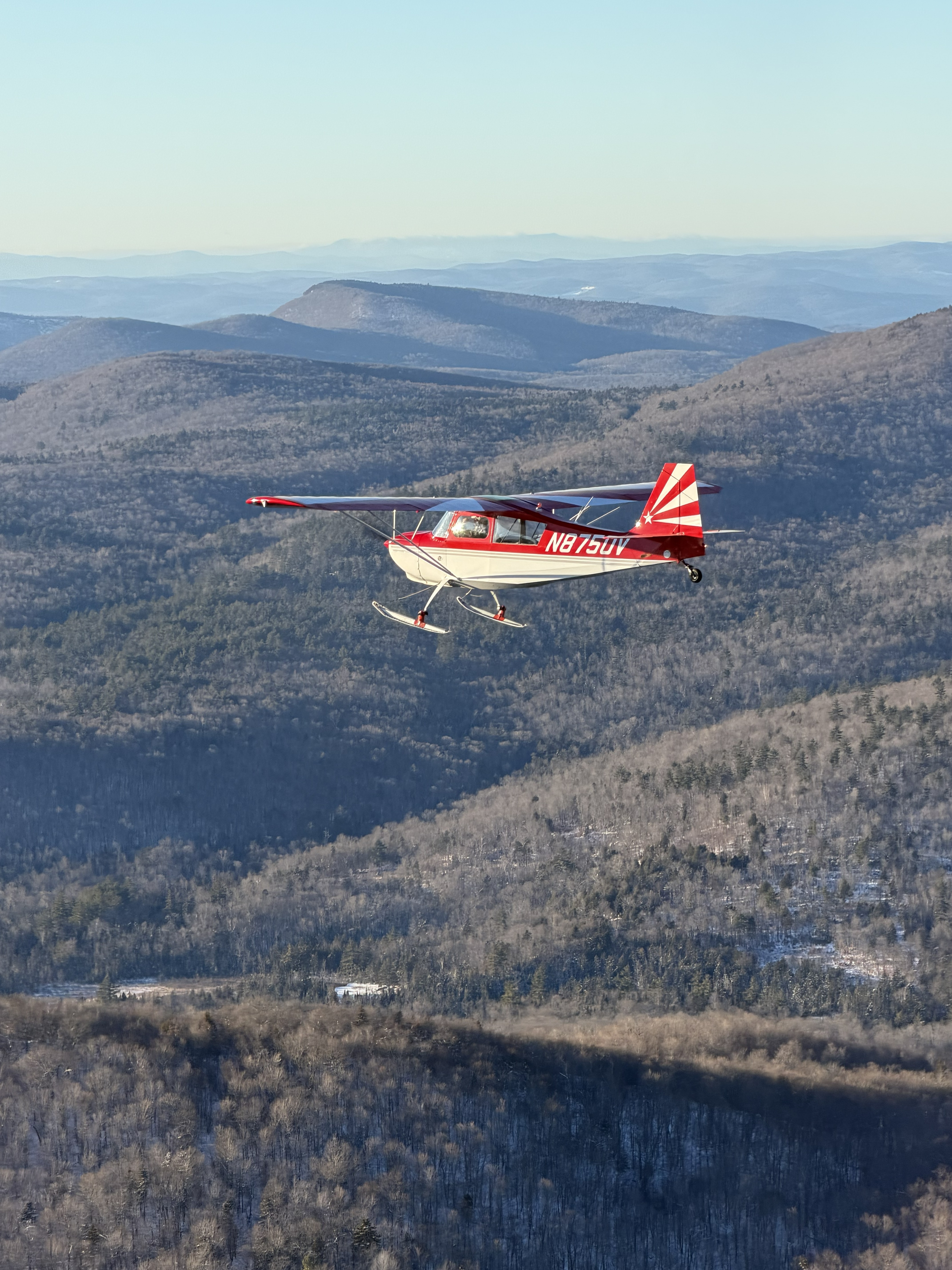 Red and white biplane N875UV flying over the Vermont mountains in winter